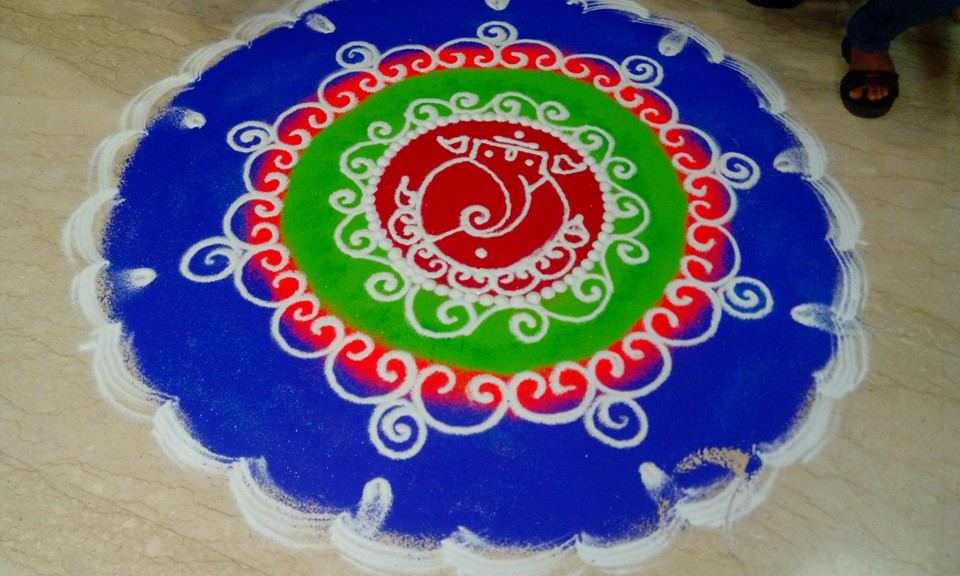 Woman in red drawing a floral rangoli